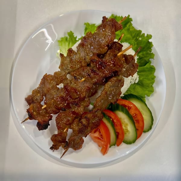 Grilled meat skewers with rice, lettuce, sliced tomatoes, and cucumbers on a white plate.