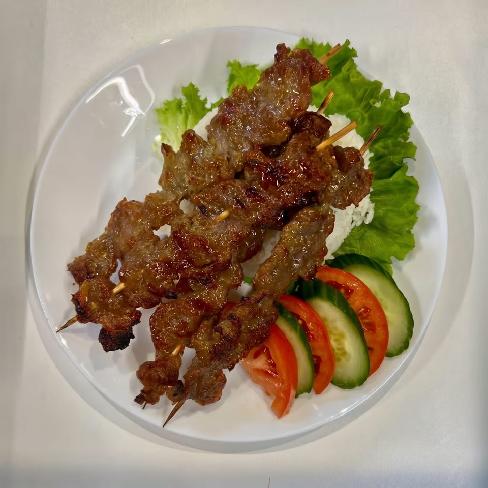 Grilled meat skewers with rice, lettuce, sliced tomatoes, and cucumbers on a white plate.
