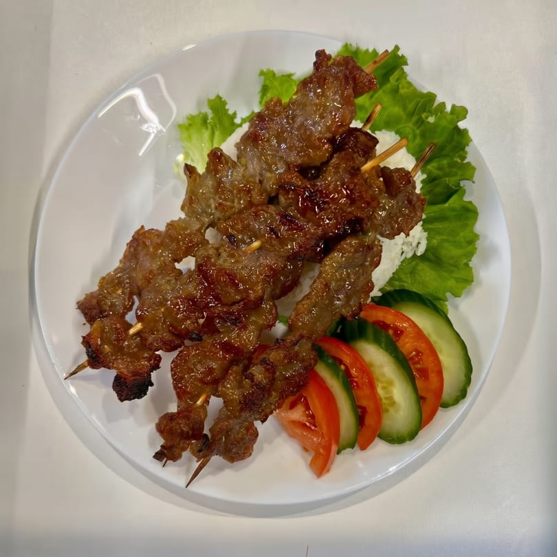Grilled meat skewers with rice, lettuce, sliced tomatoes, and cucumbers on a white plate.