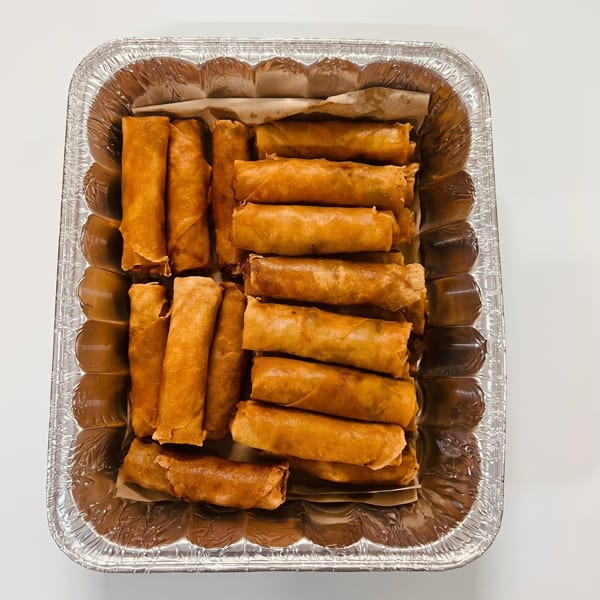 Golden-brown fried spring rolls, or lumpia, arranged in rows within a foil catering pan.