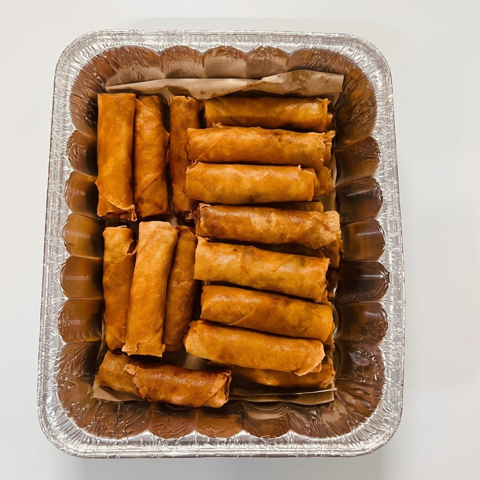 Golden-brown fried spring rolls, or lumpia, arranged in rows within a foil catering pan.