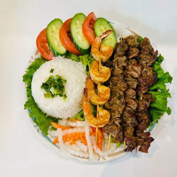 A Vietnamese dish with grilled beef and shrimp skewers, rice, pickled vegetables, and fresh salad.