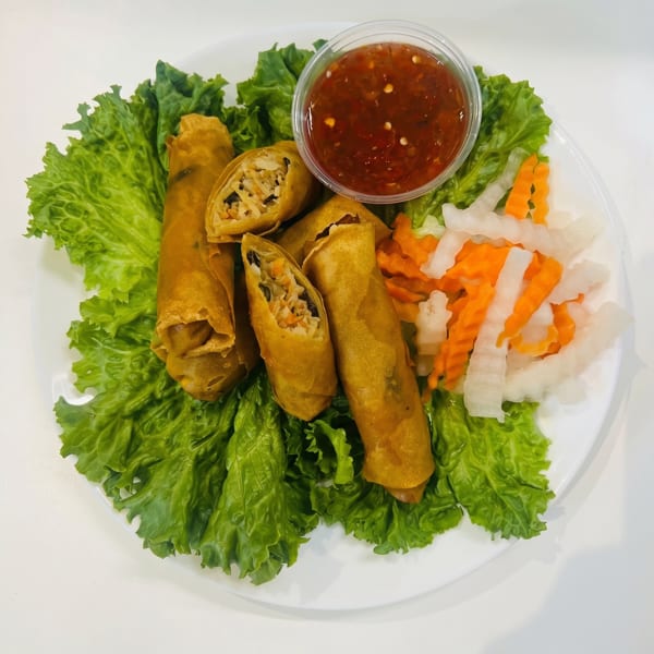 Crispy golden spring rolls, one cut open, with lettuce, pickled vegetables, and dipping sauce.