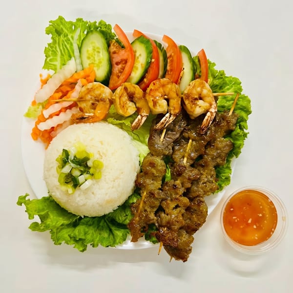 Grilled shrimp and beef skewers with rice, lettuce, cucumber, tomatoes, and pickled vegetables.