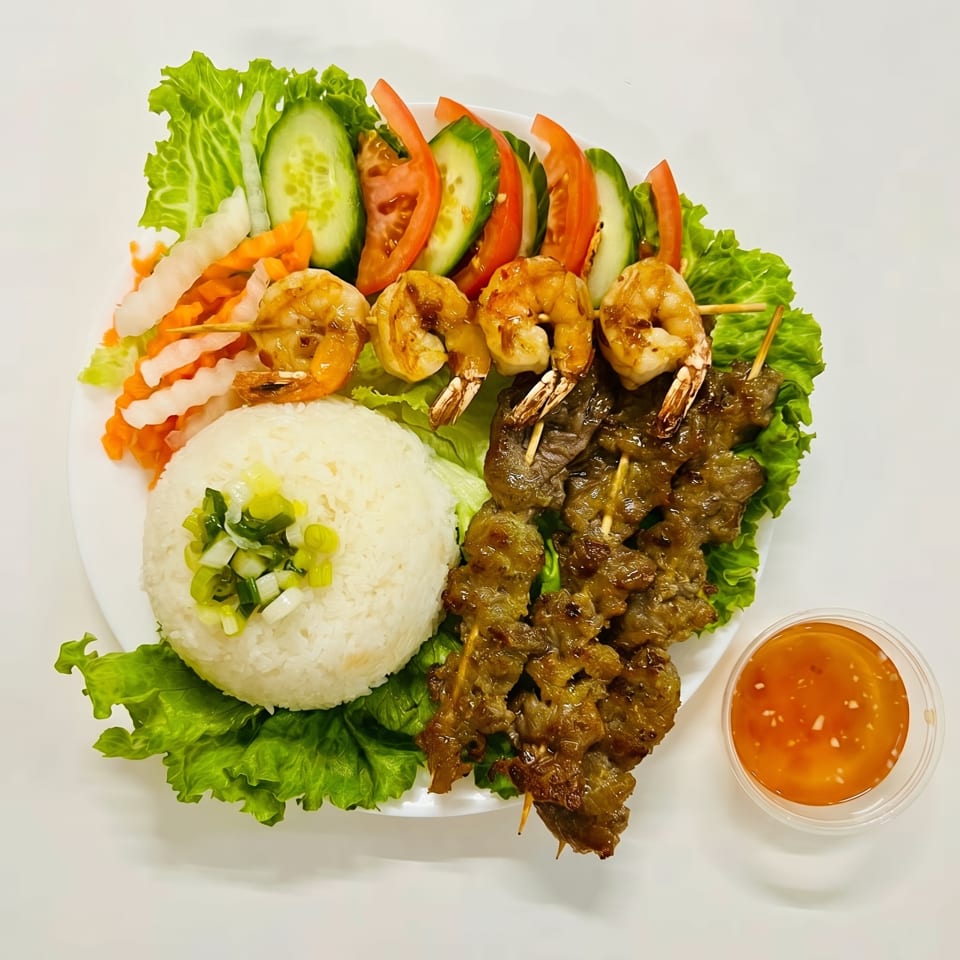 Grilled shrimp and beef skewers with rice, lettuce, cucumber, tomatoes, and pickled vegetables.