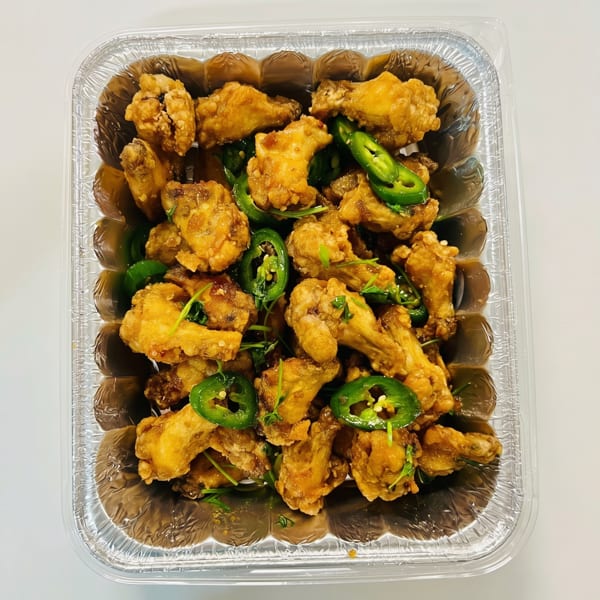 Crispy fried chicken wings with sliced green jalapeños and herbs in a foil takeout container.